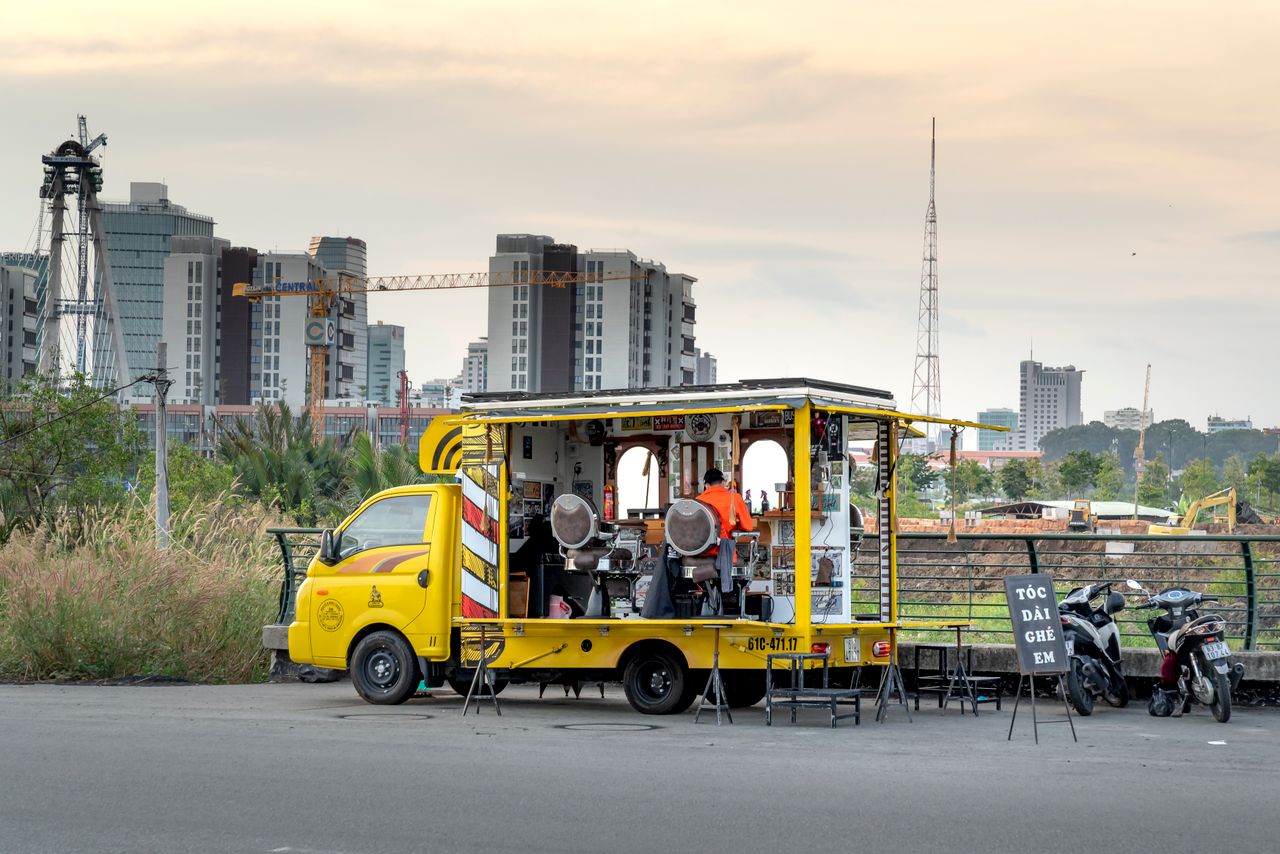 Unique mobile barbershop setup on street with urban skyline backdrop, capturing modern city life.