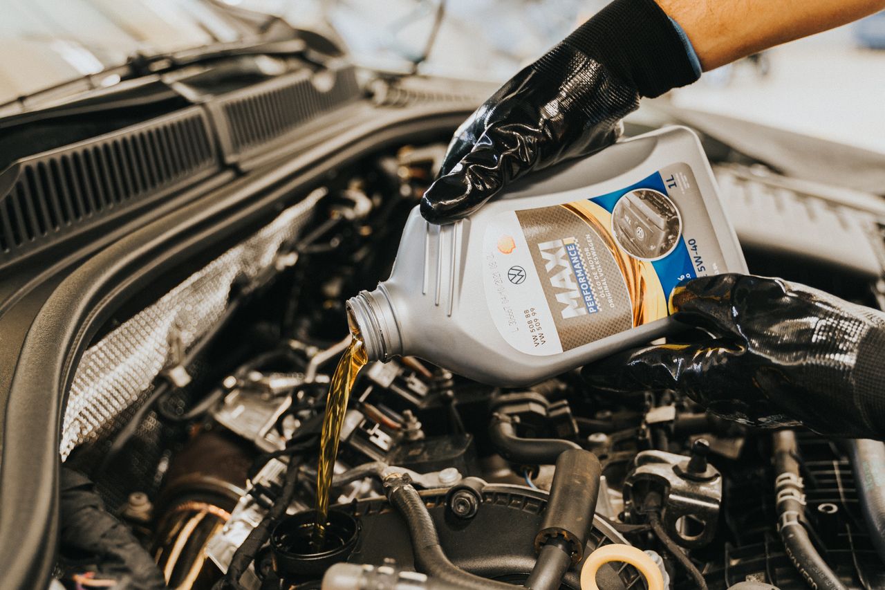 Mastering the First Impression: Your intriguing post title goes here A mechanic wearing gloves pouring oil into a car engine in a garage setting.
