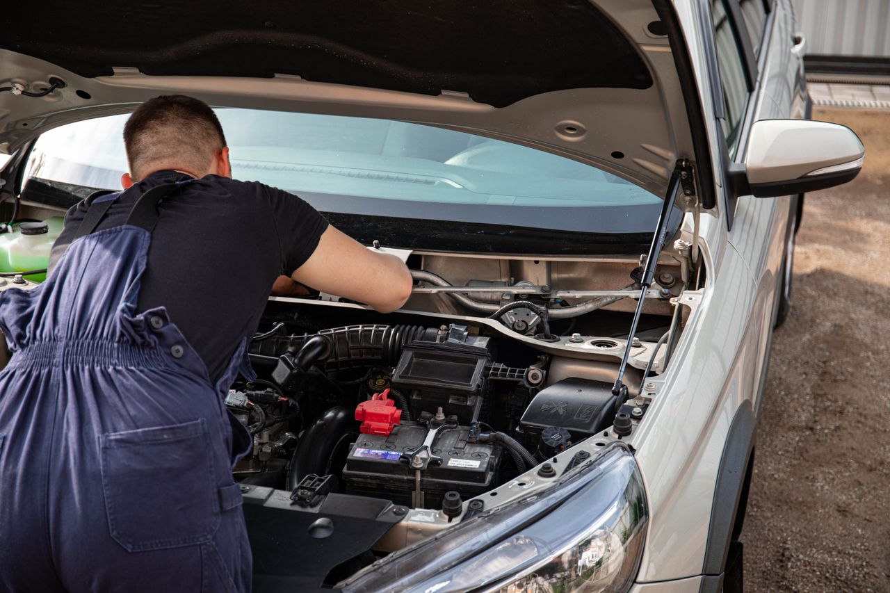 Services A mechanic fixes a car engine outdoors, focusing on vehicle maintenance.