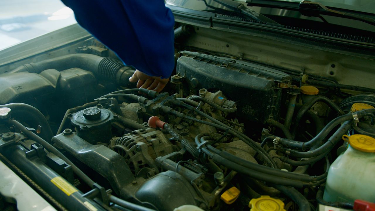 Services Mechanic in blue uniform working on a car engine in a garage environment.